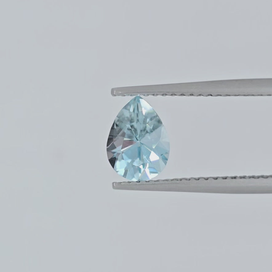 Video of a pear shaped faceted light blue gemstone in tweezers against a light background