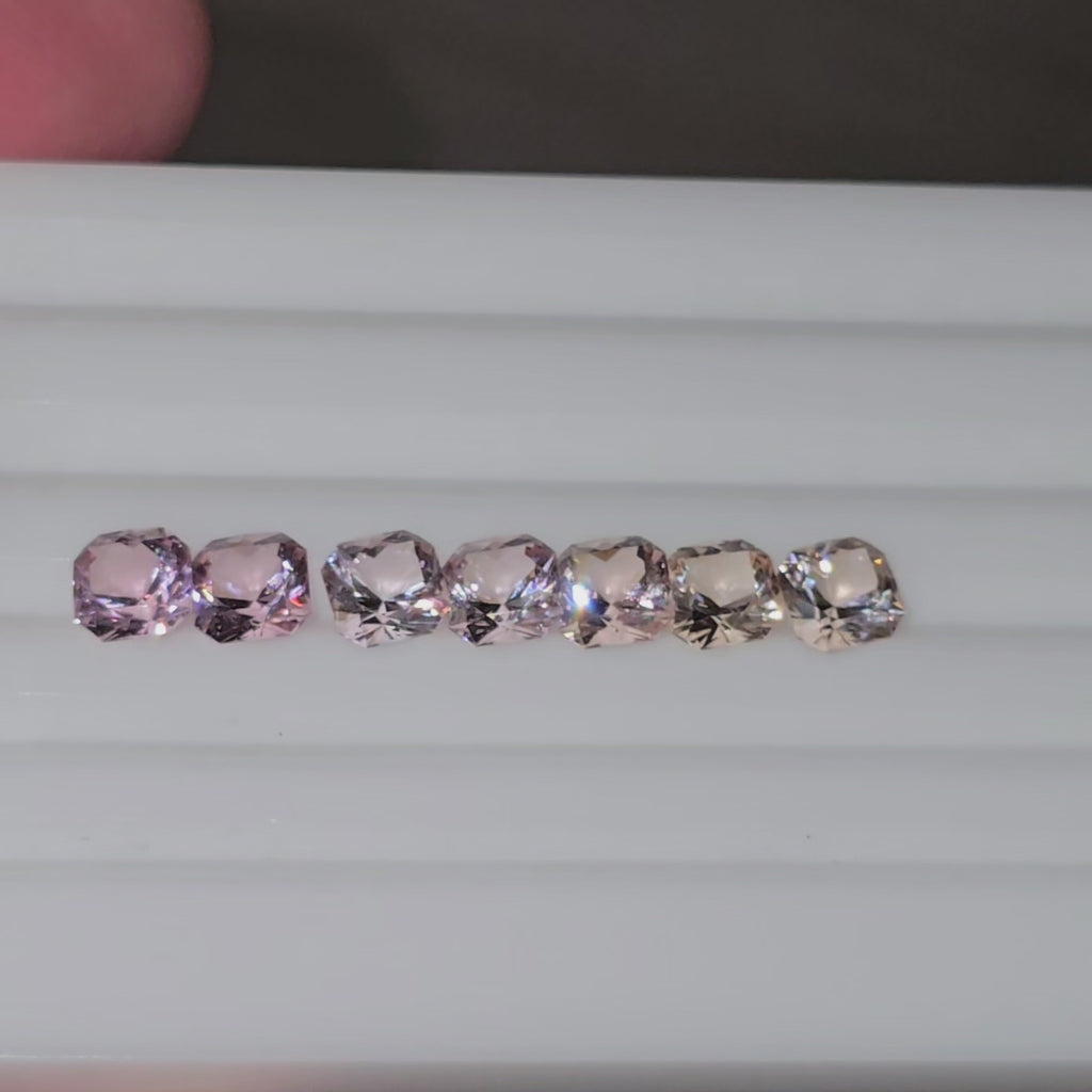 Video of seven square cut pink to pinkish orange gemstones in a line on a white background