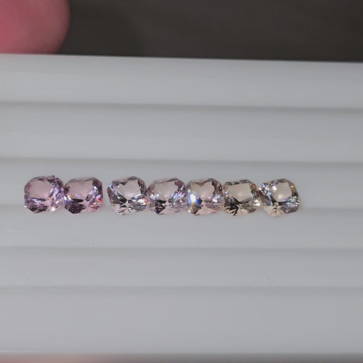 Video of seven square cut pink to pinkish orange gemstones in a line on a white background