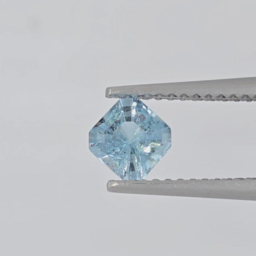 Video of a square cut blue gemstone in tweezers against a white background