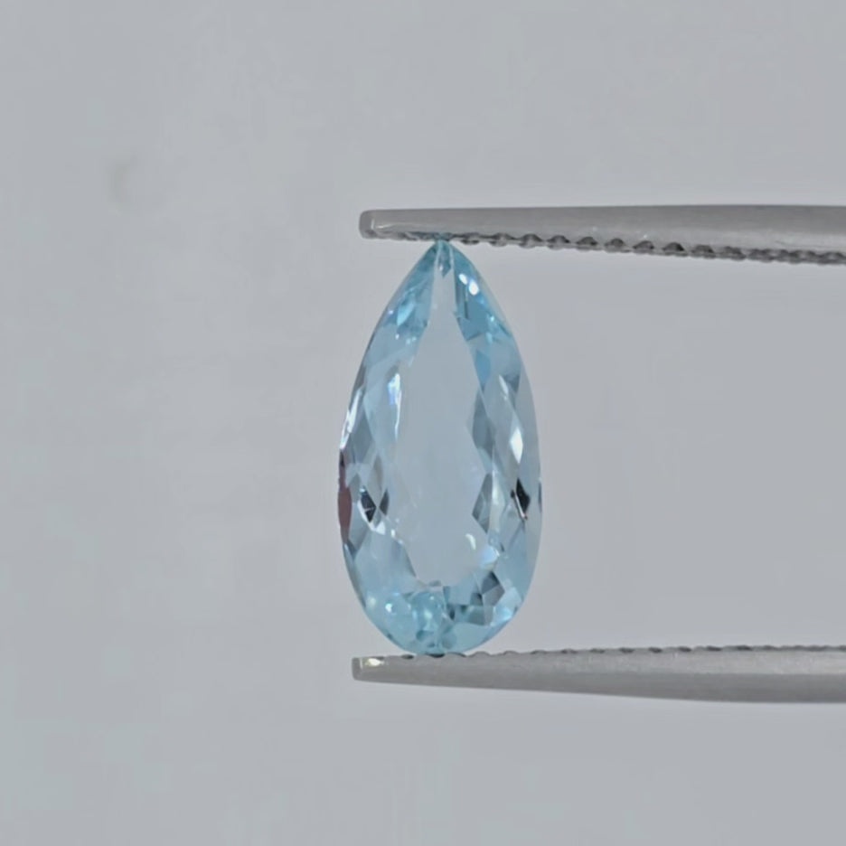 Video of a light blue faceted pear shaped gemstone in tweezers on a plain white background