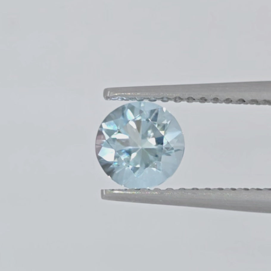 Video of a round light blue gemstone in tweezers against a light gray background