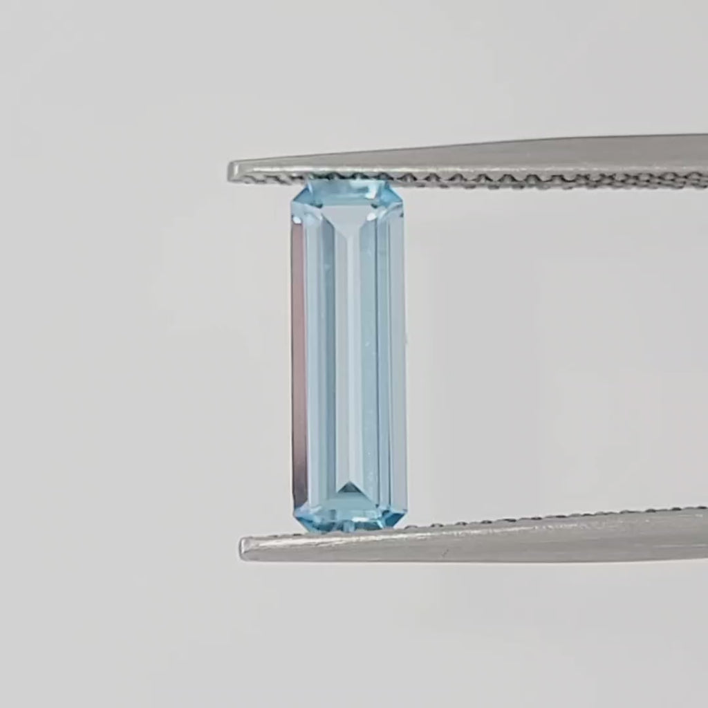 Video of an emerald cut light blue gemstone in tweezers against a white background