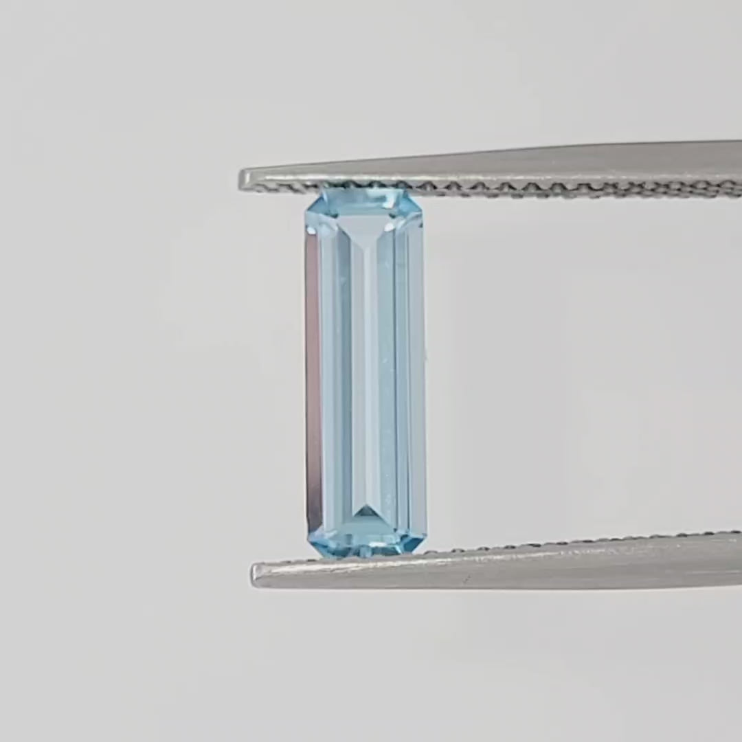 Video of an emerald cut light blue gemstone in tweezers against a white background