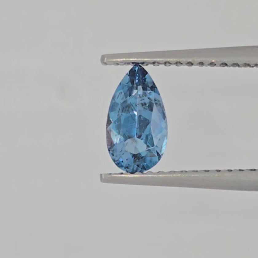 Video of a pear shaped blue gemstone in tweezers against a white background