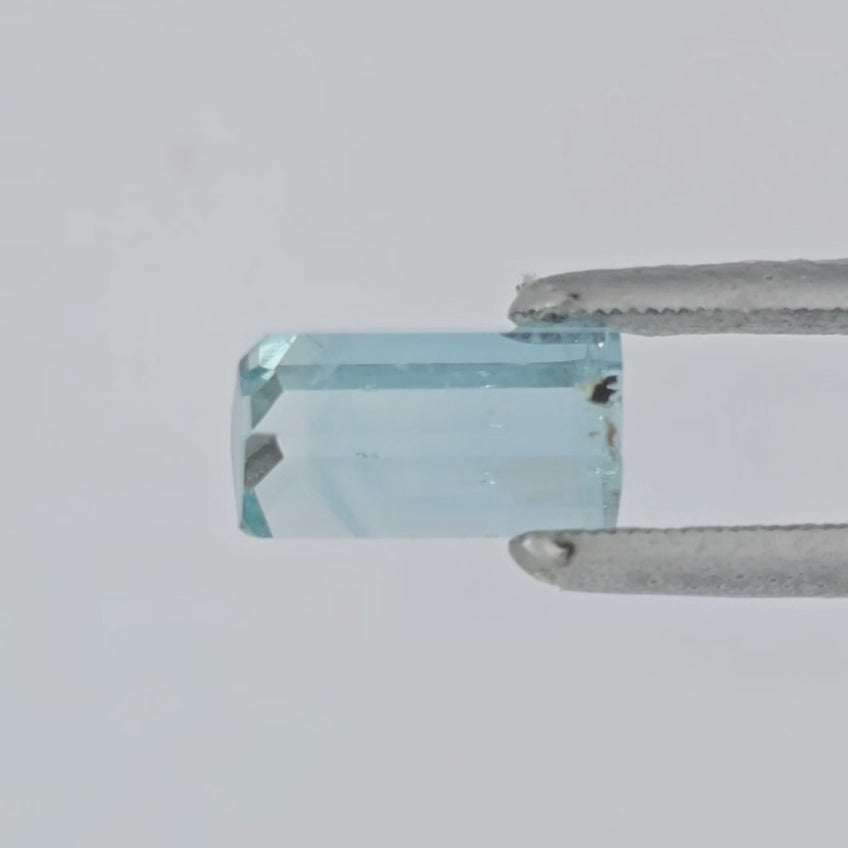 Video of light blue, transparent aquamarine crystal in tweezers against a white background