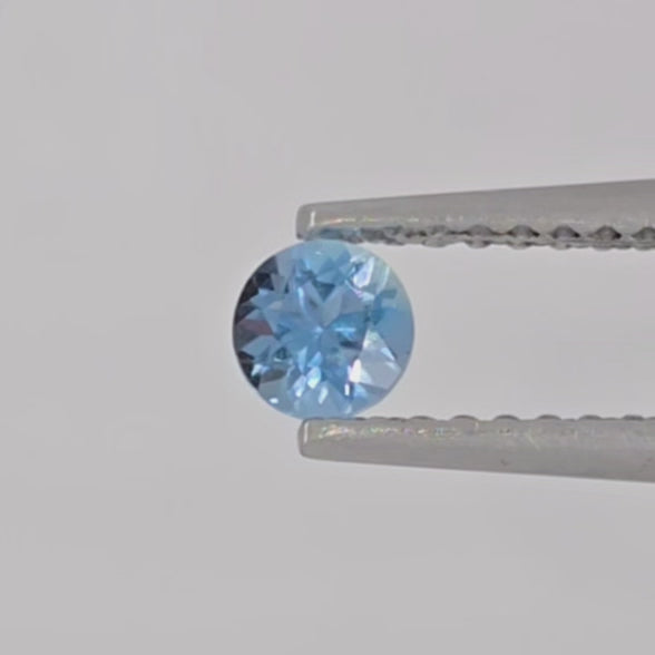 Video of a faceted round blue gemstone in tweezers against a light gray background