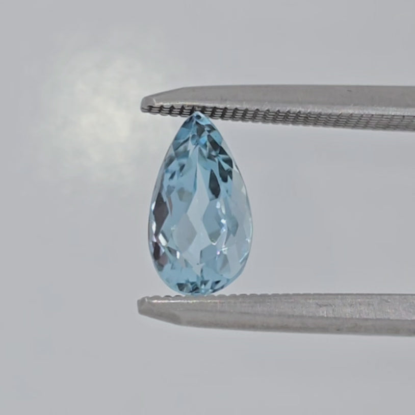 Video of a light blue pear shaped faceted gemstone in tweezers against a white background