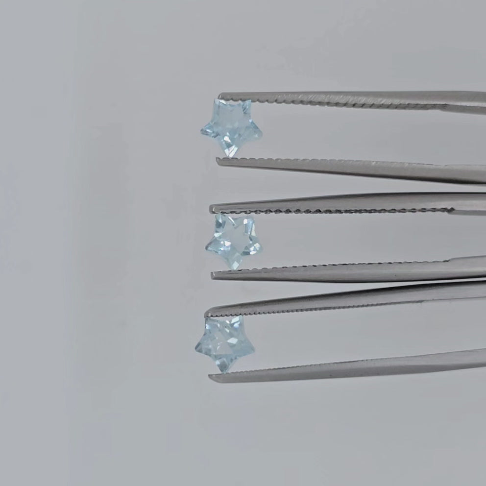 Video of three faceted star shaped light blue gemstones in tweezers against a light gray background
