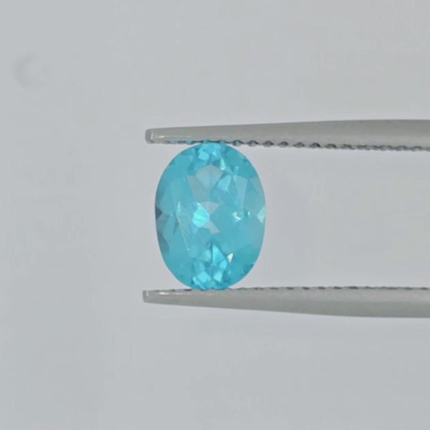 A video of a faceted oval-cut light blue gemstone shown in tweezers on a light gray background