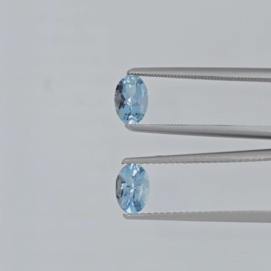 Video of two light blue oval faceted gemstones in tweezers against a plain white backgorund