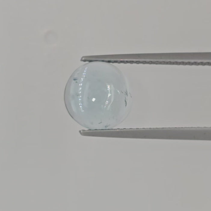 Video of a round light blue domed gemstone in tweezers against a light background