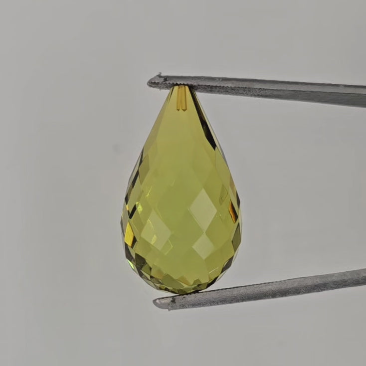 Video of a teardrop shaped yellowish green bead in tweezers against a light gray background