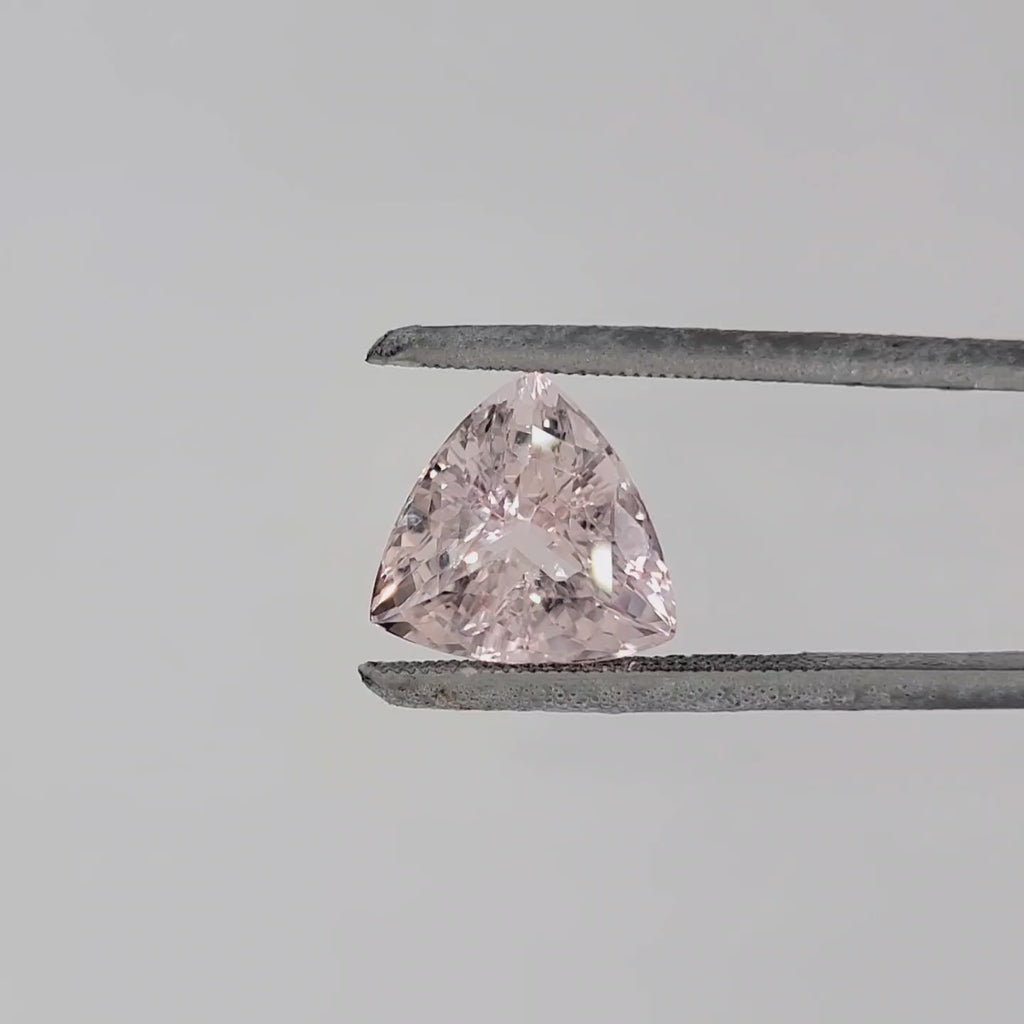 Video of a triangular shaped faceted pink gemstone in tweezers against a pale gray background
