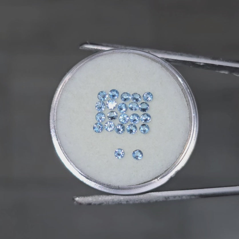 Video of small round blue gemstones on a circular white surface in tweezers against a dark gray background